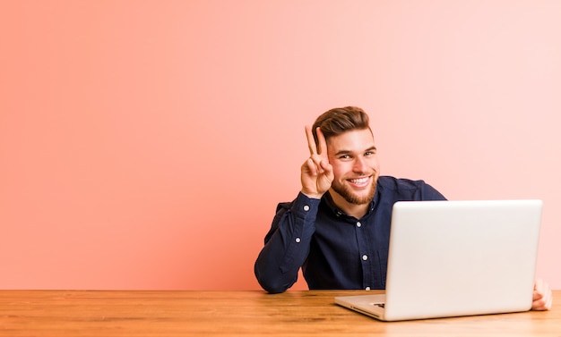 Young man working with his laptop showing victory sign and smiling broadly.