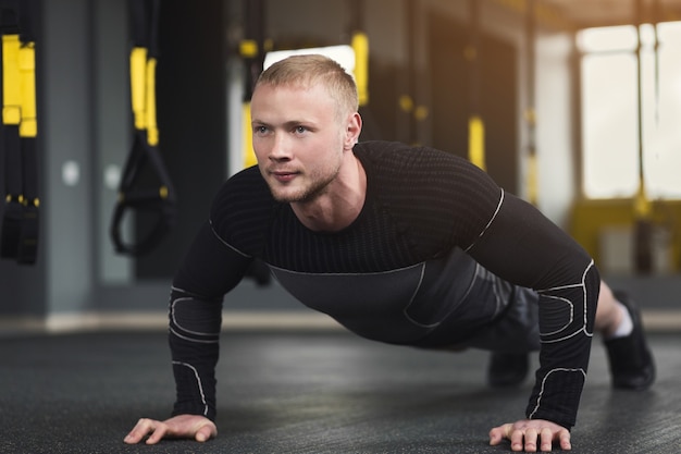 Young man workout in fitness club. Closeup portrait of caucasian guy making plank or push ups exercise, training indoors, copy space