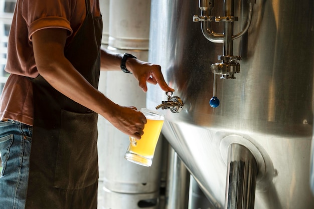 Un giovane lavora in un birrificio e controlla la qualità della birra artigianale il proprietario del birrificio assaggia le migliori birre di bach la scorciatoia di un uomo riempie un bicchiere di birra con