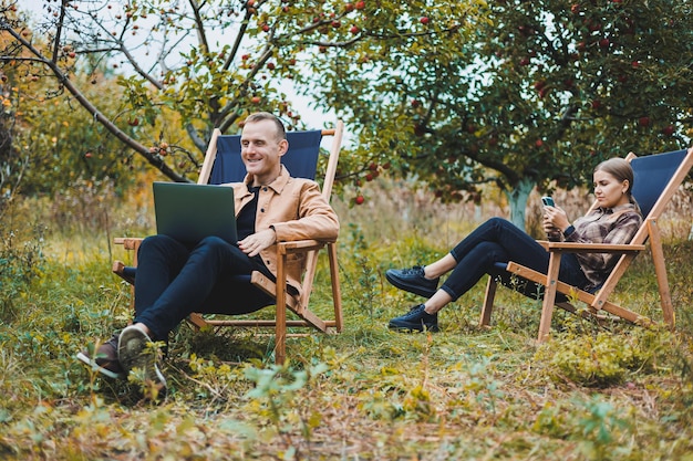 A young man works in the garden outdoors while sitting in a comfortable garden chair Remote work on a portable laptop