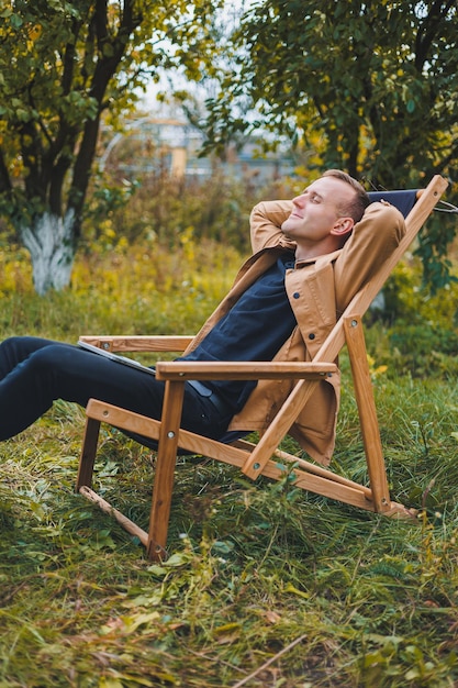 A young man works on a laptop outdoors A young freelancer rests in the forest Remote work active recreation in the summer Tourism people concept man sitting on a chair outdoors