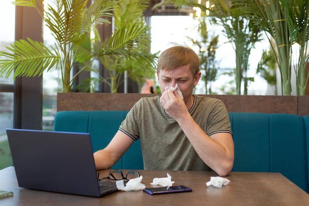 A young man works online gets sick wipes his nose with a napkin is allergic to flowers and plants