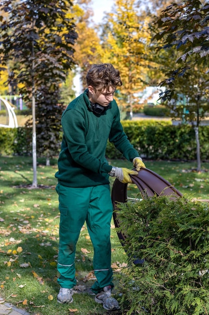 若い男が花屋、ランドス ケープ デザイナーまたは庭師として公園で働いています。エコロジーの概念