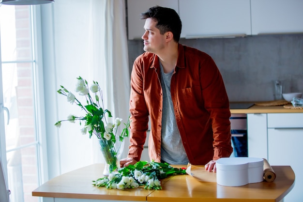 Young man wrapping wite roses on a table at kitchen. Own business concept