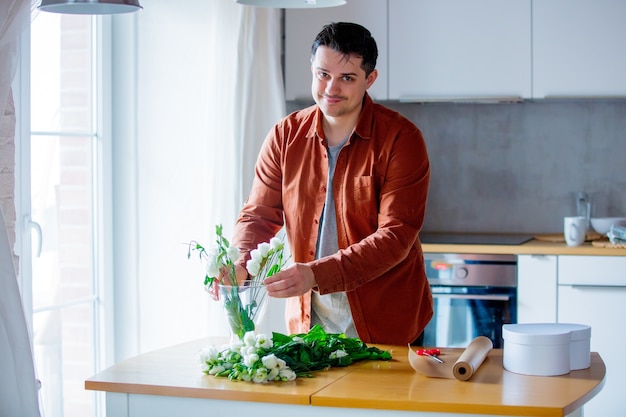 Young man wrapping wite roses on a table at kitchen. Own business concept