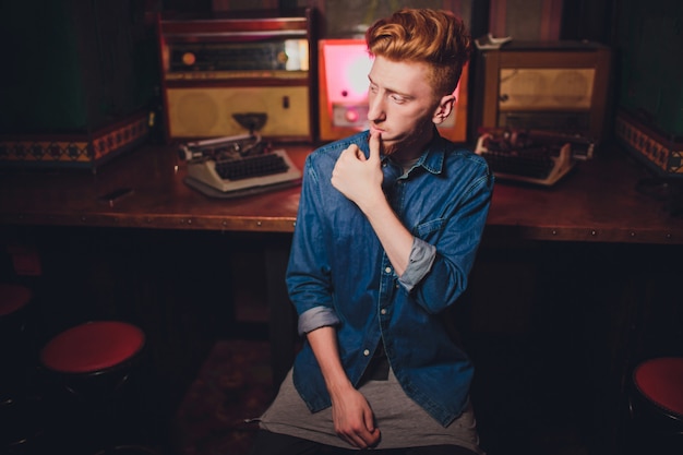 Young man writing on old typewriter. in dark lighting, restaurant, modern clothes, old writer habits