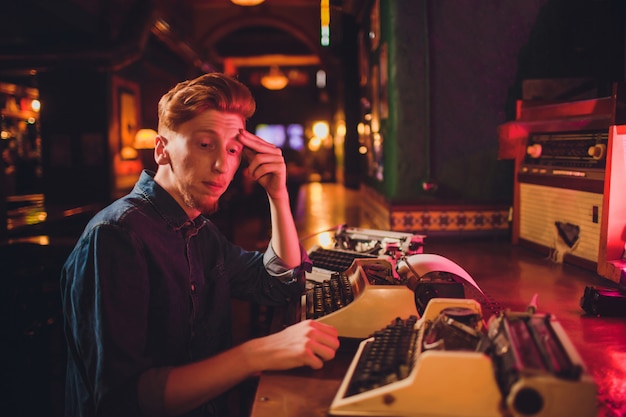Молодой человек, писать на старой пишущей машинке. в темном освещении, ресторан, современная одежда, старые писательские привычки