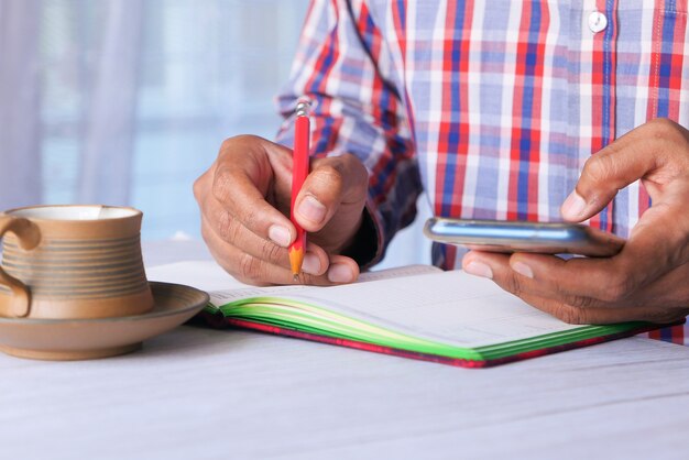 Young man writing and using smart phone on office desk