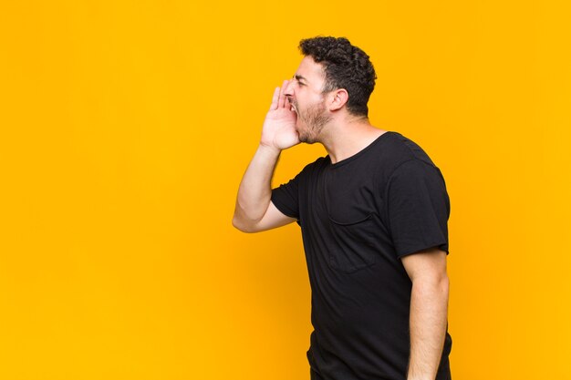 Young man yelling loudly and angrily to copy space on the side, with hand next to mouth