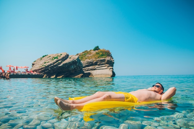 Young man at yellow inflatable mattress in clear transparent water