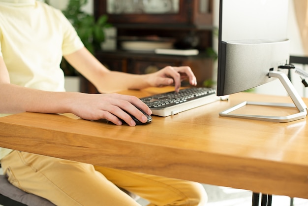 young man in a yellow t-shirt works at home at the computer. chat online. remote work via the Internet on isolation during quarantine of the coronavirus. freelancer