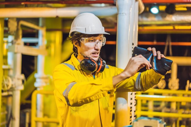 Young man in a yellow work uniform glasses and helmet in industrial environmentoil platform or