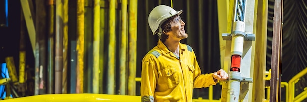 Young man in a yellow work uniform glasses and helmet in industrial environmentoil platform or