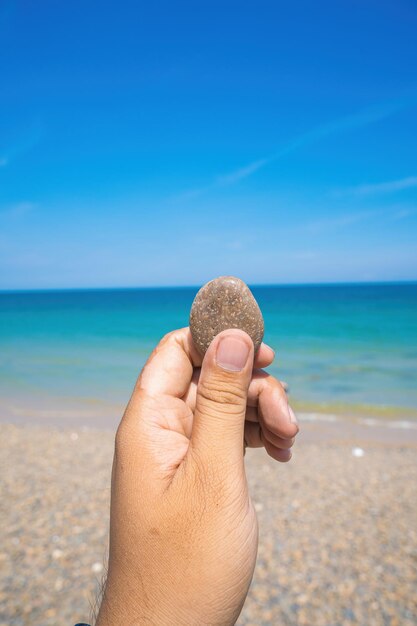 海の前にカラフルな石を持っている若い man39s 手 夏の日の旅行と休暇の概念のビーチで素晴らしい風景の背景に青い小石石を手に