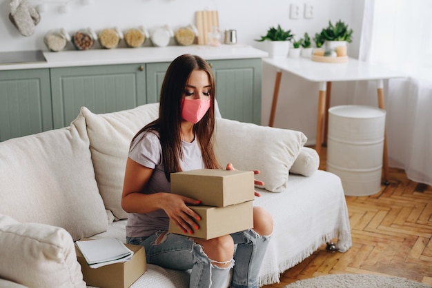 Young manager girl sits on sofa makes online orders in mask at home Safe online delivery concept