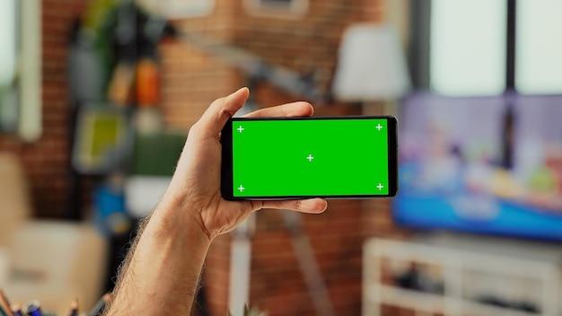 Young manager holding telephone with horizontal greenscreen\
template on digital screen, looking at isolated display. using\
blank chroma key copyspace and mockup on smartphone. close up.