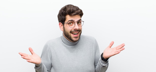 Young manager man feeling happy, excited, surprised or shocked, smiling and astonished at something unbelievable against white wall