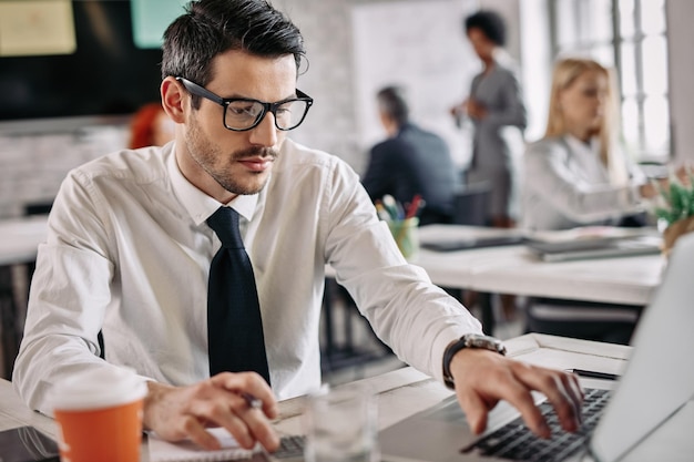 Young manager using laptop while calculating financial reports in the office There are people in the background