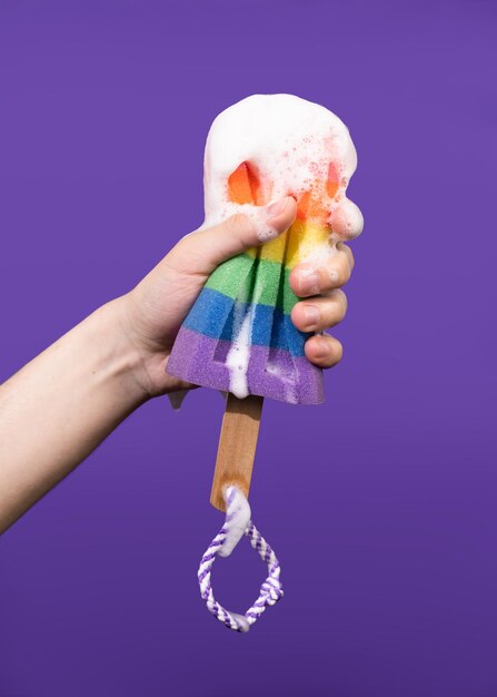 Young mans hand holds rainbow colored foam sponge on a purple background