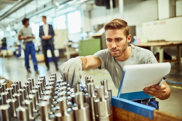 Young manual worker examining manufactured rod cylinders while working in a factory