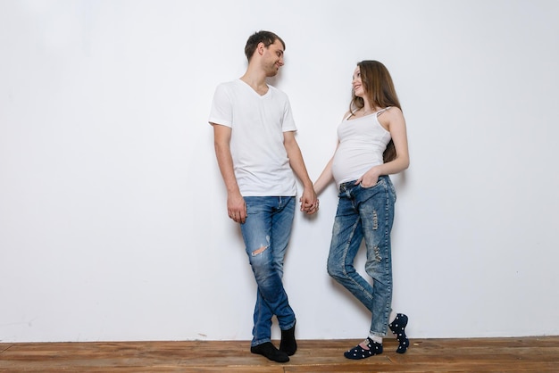 La giovane coppia sposata abbraccia in piedi vicino al muro bianco. mostra un'istantanea di un'ecografia. il marito tiene la mano della moglie incinta. una coppia di innamorati, futuri genitori. stile di vita, persone felici.