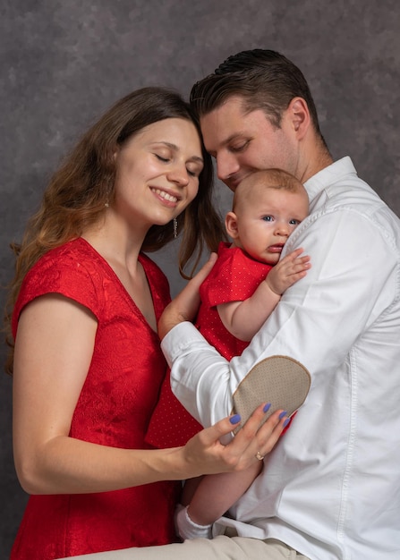 A young married couple like parents hold their little daughter in their arms standing next to eac