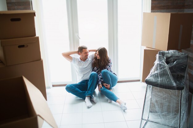 A young married couple in the living room in the house are sitting near the window. they are happy about new home. Moving, buying a house, apartment concept.