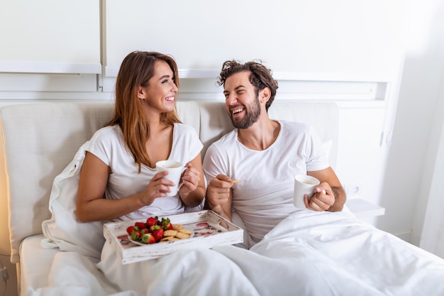 Young married couple in love eating breakfast in their bed. Good morning! Healthy breakfast in bed. Young beautiful love couple is having breakfast in bed.