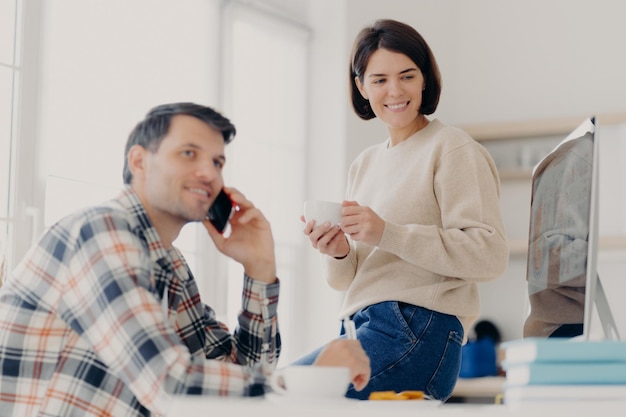 Young married couple study contract for new house check\
documents for buying property man discusses something with partner\
via cellphone happy woman drinks tea and looks in computer\
monitor