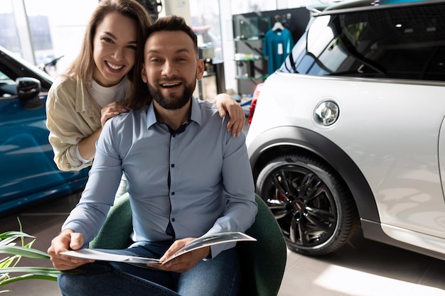 Молодая супружеская пара изучает буклет перед покупкой нового автомобиля с концепцией личного транспорта