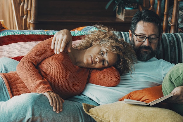 Photo young mature couple at home having relax and resting together on the sofa man reading a book and woman sleeping on him love and life relationship concept bored people indoor leisure activity