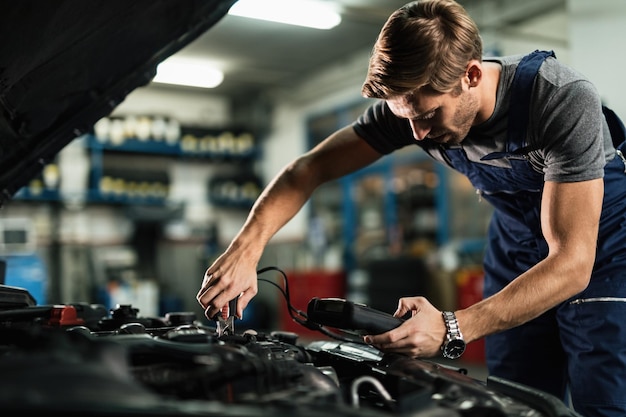 Young mechanic examining car battery with diagnostic tool while working in auto repair shop