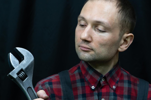 A young mechanic in a fashionable checked vest a large wrench\
in the hand of a car repair specialist builder with a tool on a\
black background studio photography