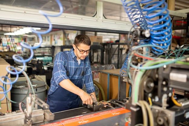 Young mechanic of modern production factory examining one of industrial machines or repairing it