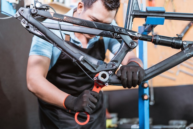 A young mechanic wears gloves using a bottom bracket wrench to lock