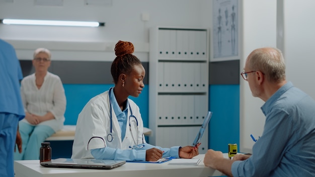 Young medic explaining x ray result to old man at desk