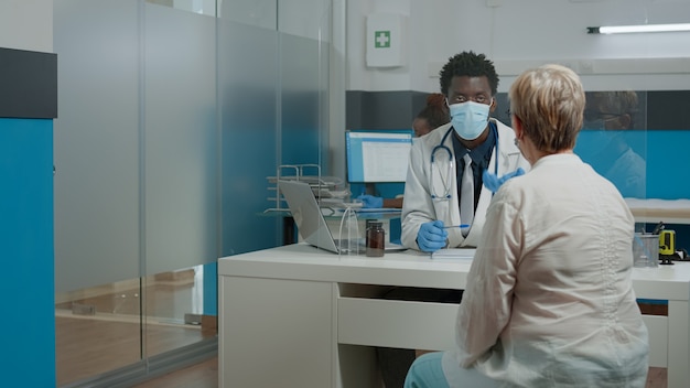 Young medic wearing face mask while consulting elder patient