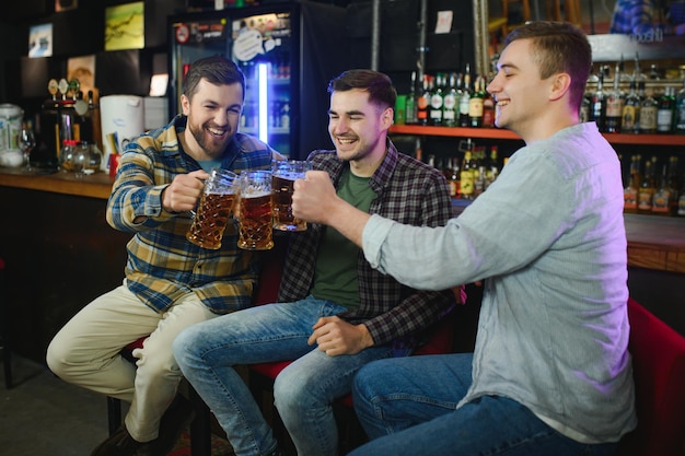 Young men in casual clothes are talking laughing and drinking while sitting at bar counter in pub