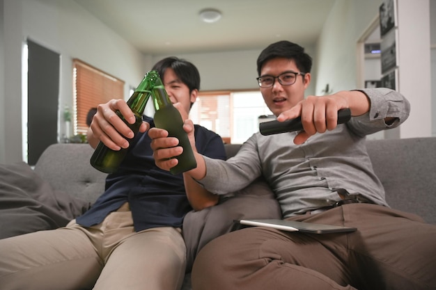 Young men clinking their glasses of beer while cheering football match at home