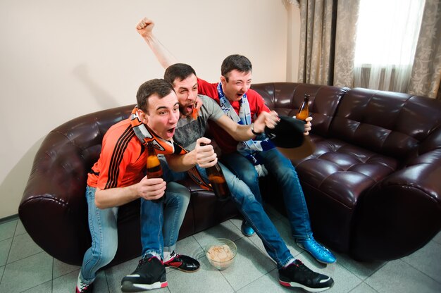 Young men drink beer, eat chips and root for football