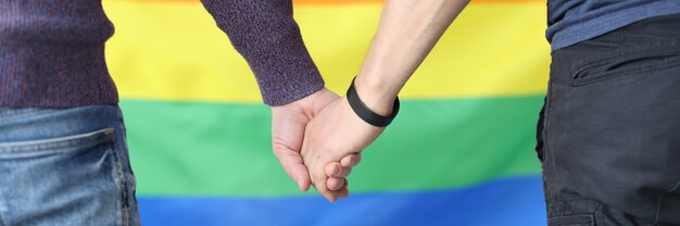 Young men holding hands with lgbt flag background closeup. Gay love concept