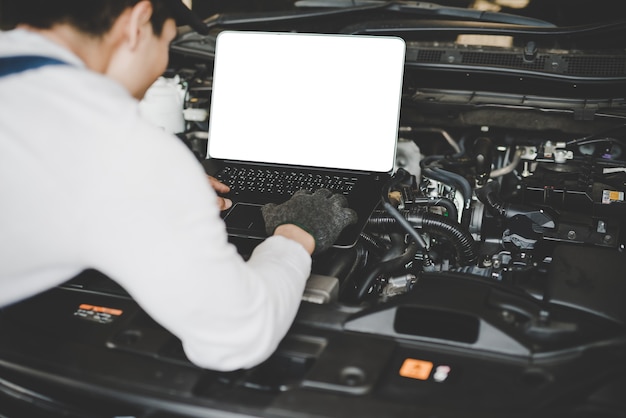 Young men mechanic working on a computer connected to a car engine