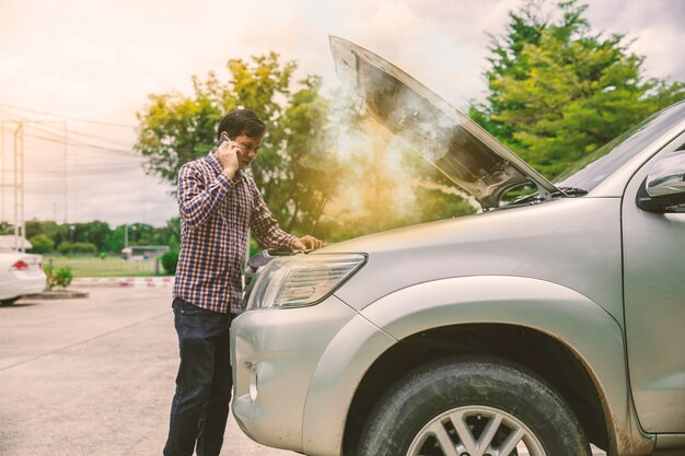 彼の壊れた車の近くの若い男性は助けを待っている。