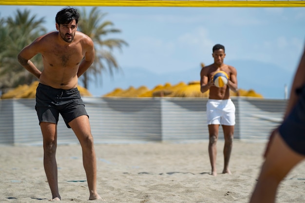 Giovani uomini che giocano a beach volley sulla spiaggia in una giornata di sole