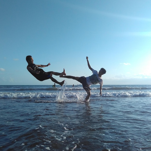 Young men playing over sea against sky