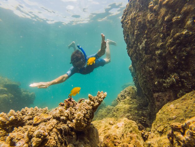 Young men snorkeling exploring underwater coral reef landscape background in the deep blue ocean with colorful fish and marine life