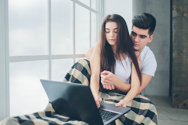 Giovani uomini e donne stanno lavorando al computer o stanno cercando informazioni su internet in una finestra inondata di luce solare