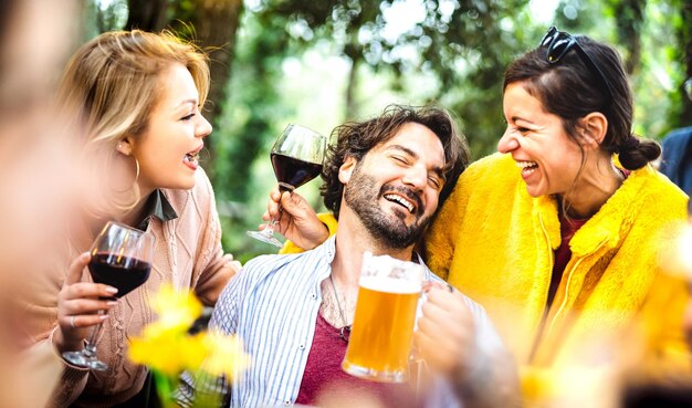 Young men and women having fun moment drinking wine and beer at garden party