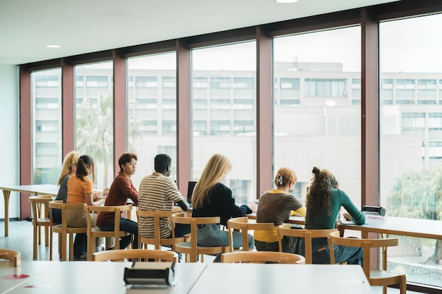 Photo young men and women sitting at table against window