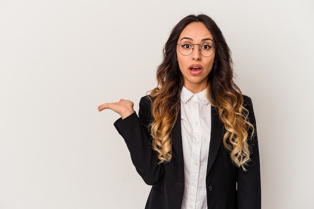 Young mexican business woman isolated on white wall impressed holding copy space on palm.